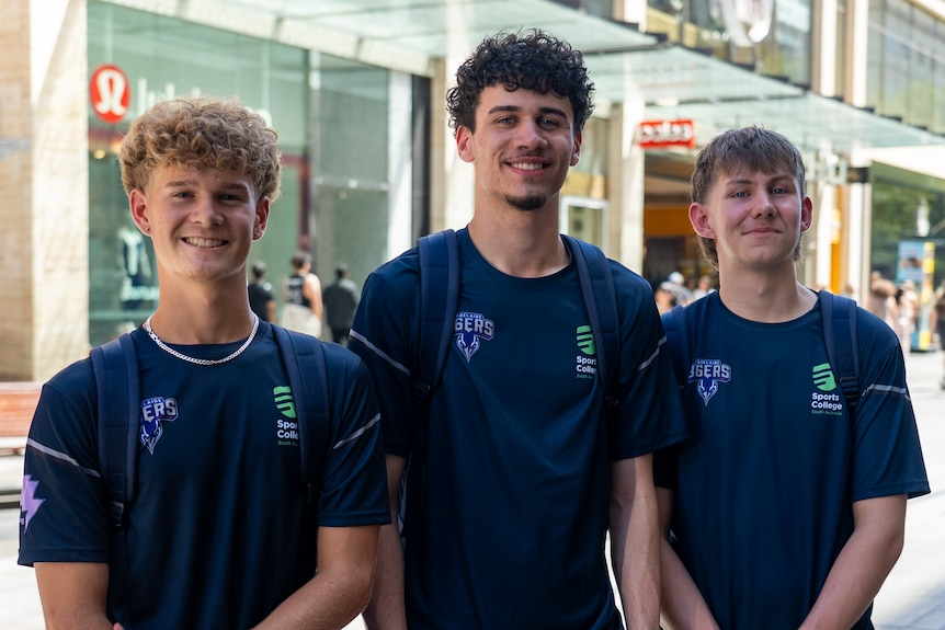 Three teenage boys waring the same navy shirt stand together smiling.
