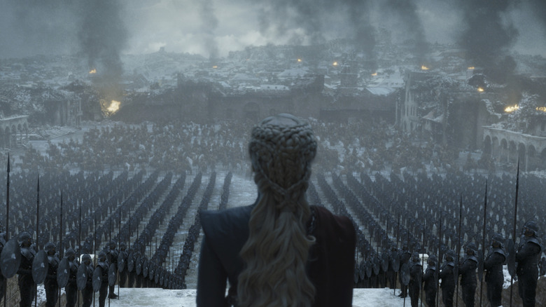 Emilia Clarke as Daenerys Targaryen standing in front of an army as a city burns in the background in Game of Thrones
