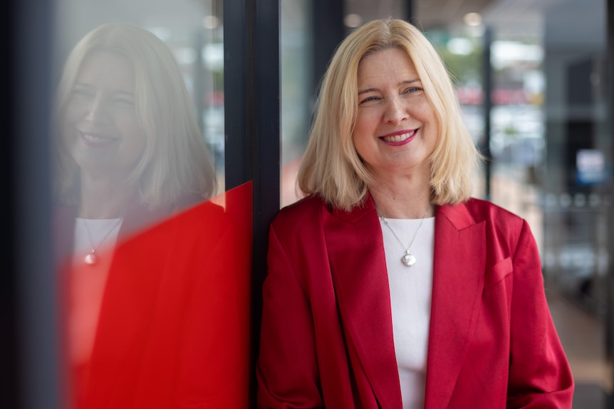 A smiling blonde woman in a brightly-coloured blazer.
