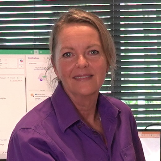 A woman sitting on a swivel chair at a desk, inside a small office.