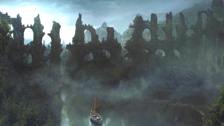 Iain Glen as Jorah Mormont sailing a small boat through a misty river with ancient ruins in the background in Game of Thrones