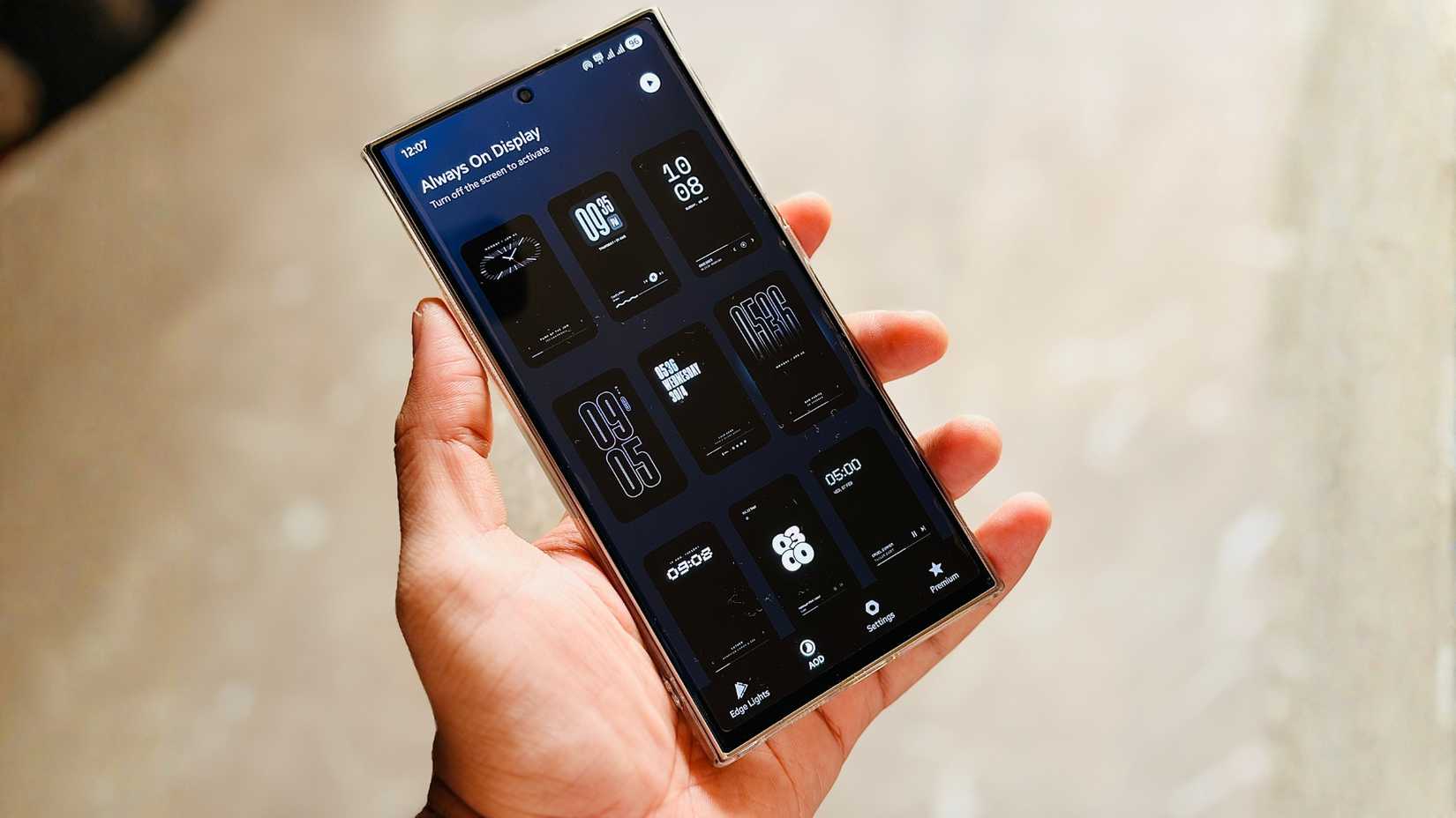 Hand holding an Android phone showing multiple Always On Display clock styles in the Muviz Edge AOD app