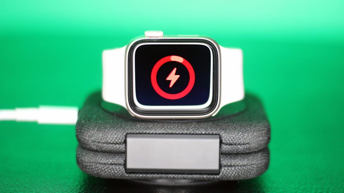Apple Watch with white band charging on a dock, with a screen indicating low battery