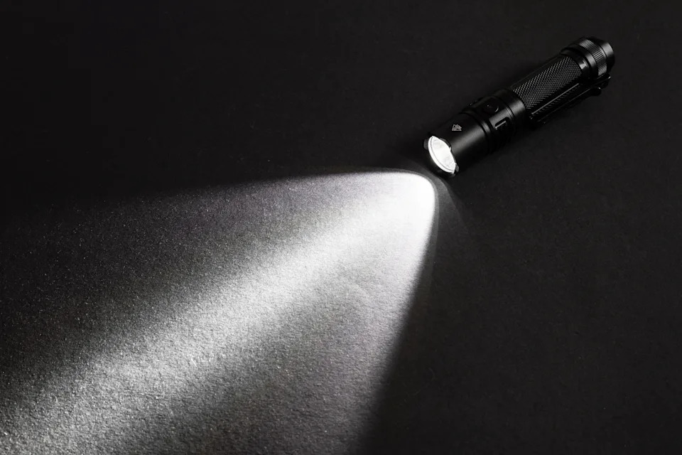 A flashlight beams light onto a dark surface, illuminating the area in a focused stream