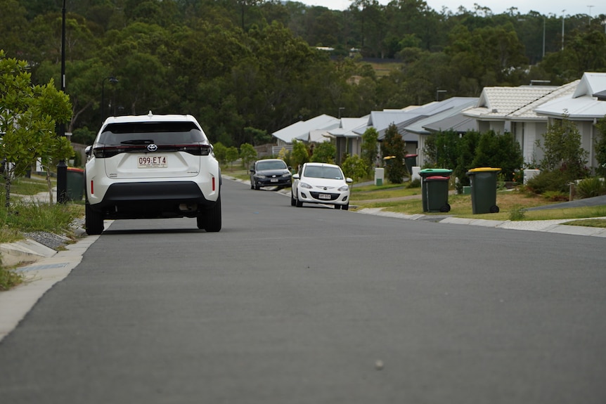 A white car is parked on a quiet and leafy suburban street