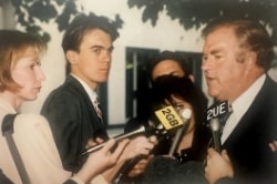 A press pack interviews a man in a suit