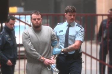 Dimitri in a grey tracksuit arrives at court in handcuffs. 