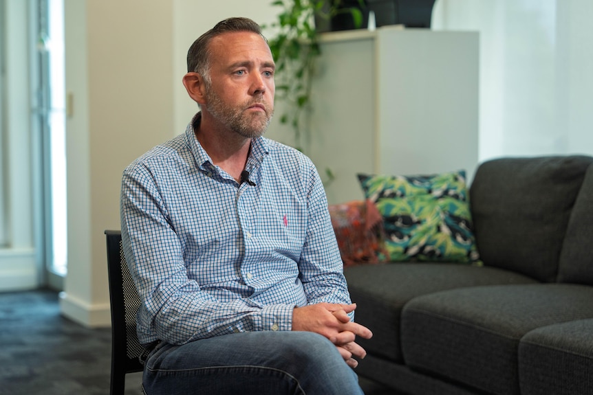 A man wearing a check shirt talks to the camera.
