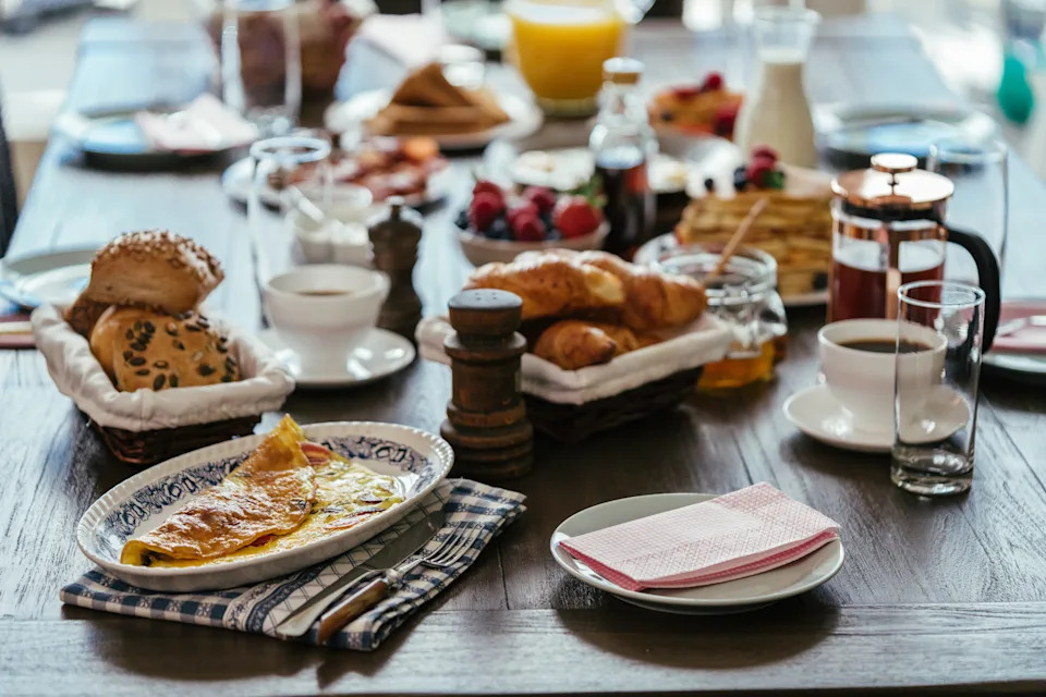 A rustic breakfast spread on a wooden table with pastries, fruit, coffee, and juice