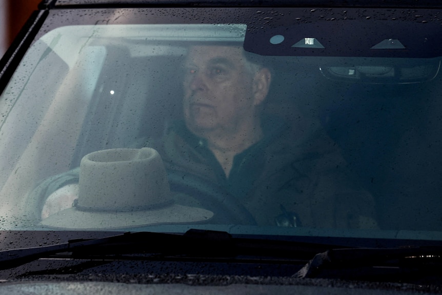 Andrew, An elderly man driving a car, the photo looks through the rainy windshield. He is serious.