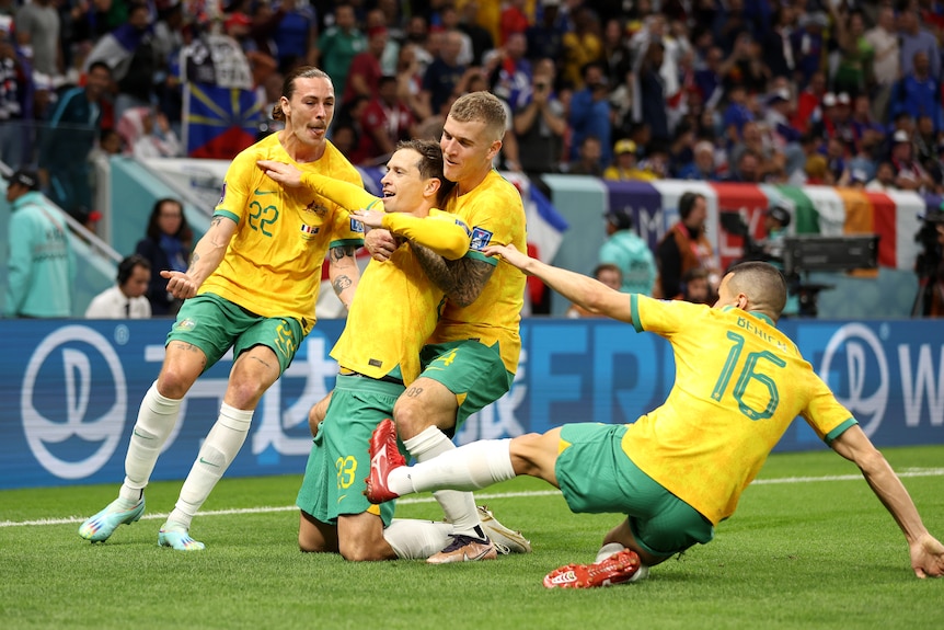 Socceroos' Craig Goodwin slides on his knees as teammates embrace him after a goal against France at the Qatar World Cup.