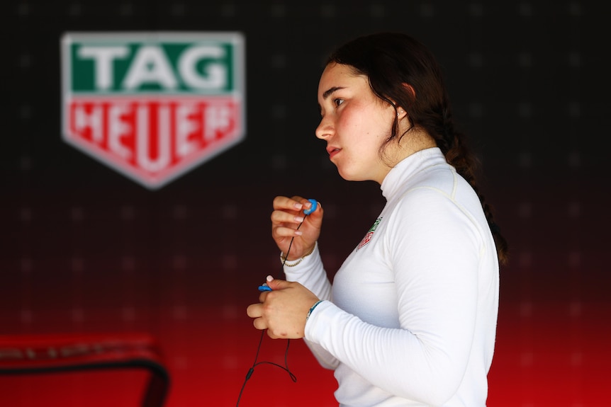 Fermale racing driver applying ear protection in the garage before driving.