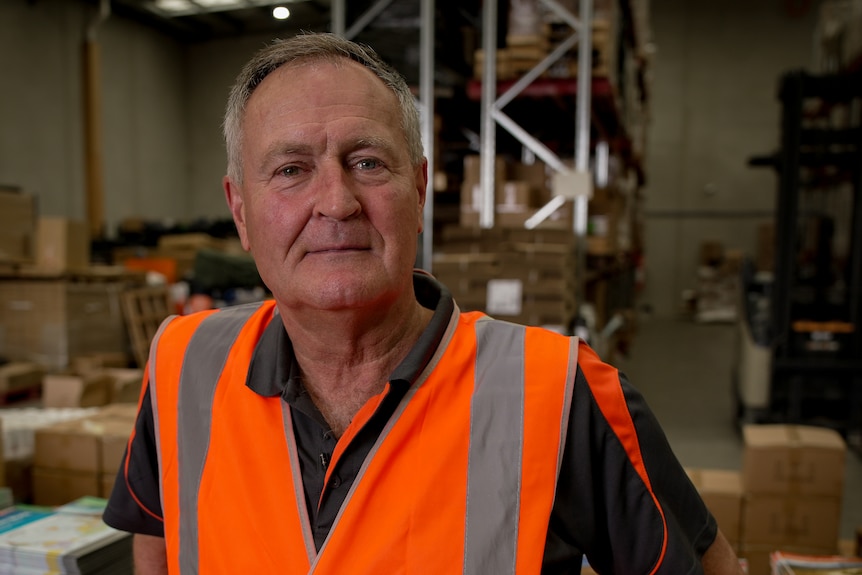 A middle-aged man in orange hi-vis vest stands in a factory