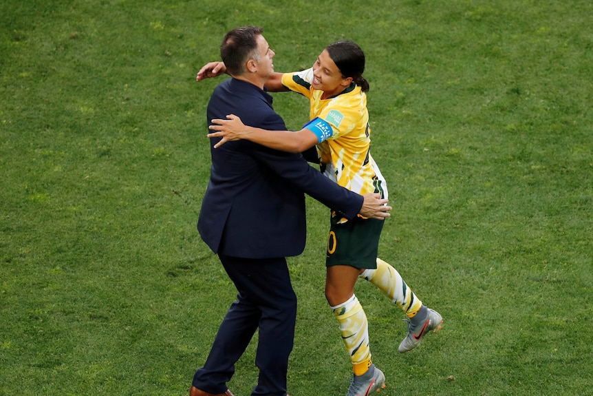 Man in suit and woman in sports gear embrace on field