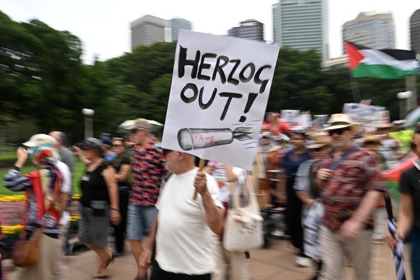 Several people taking part in a protest, including one holding a poster saying Herzog Out