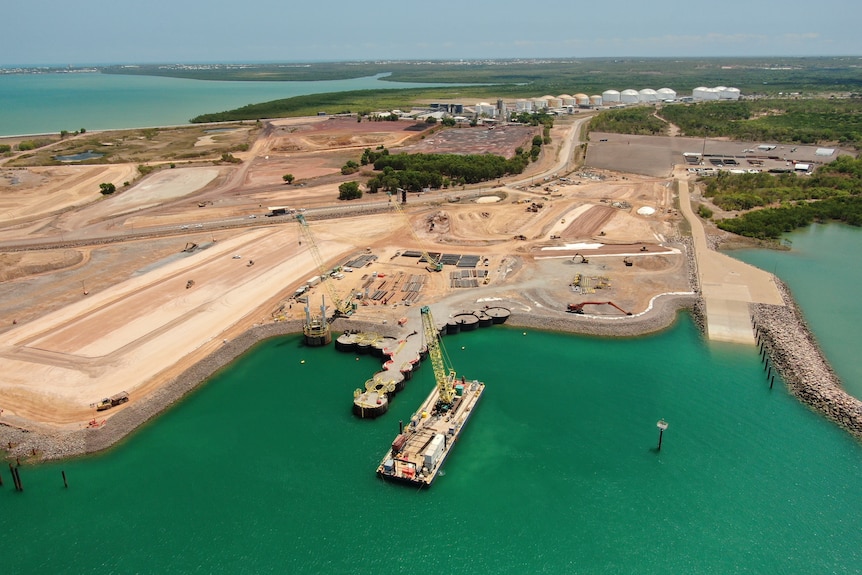 An aerial shot of a construction site near the ocean's edge, cranes can be seen below.