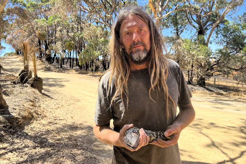 A man in a burnt out landscape holding a large sleepy lizard