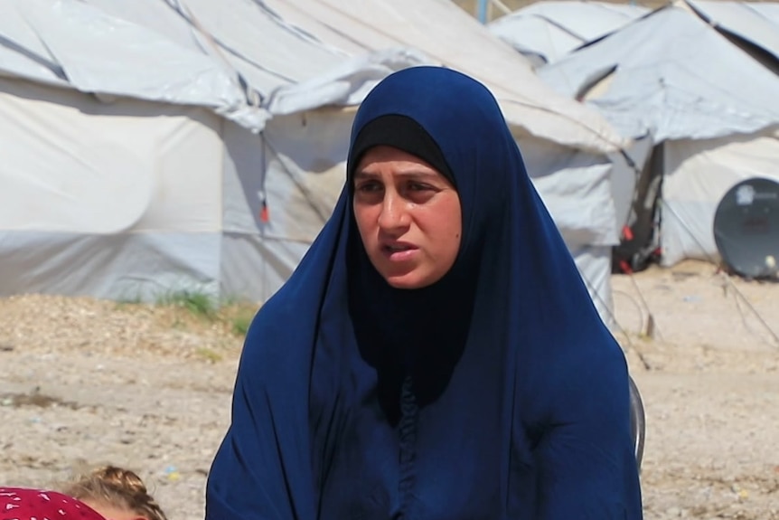 Kirsty sitting on a chair in a sandy area with white tents in the background.
