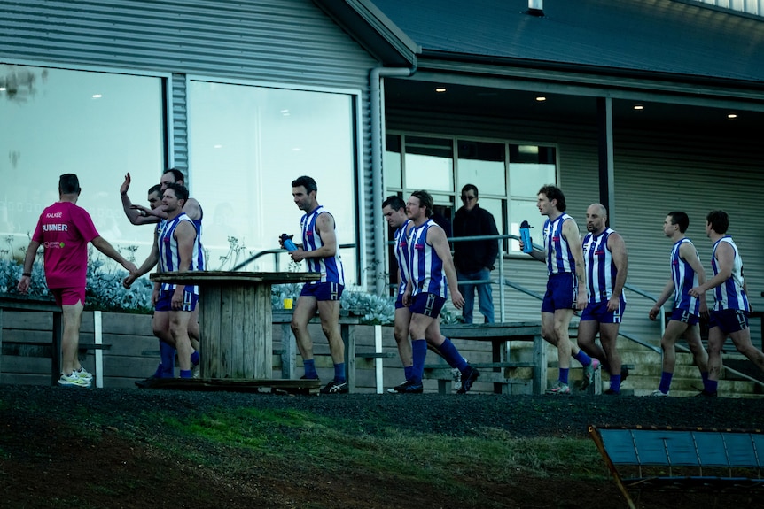 Footballers walk with a building behind them.