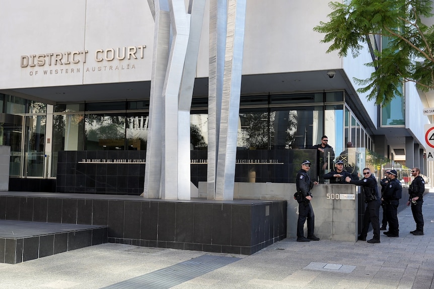 A group of seven uniformed and armed police officers standing outside the District Court of WA building in Perth's CBD.