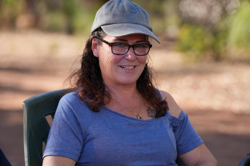 A close-up shot of a woman with dark hair wearing a cap and spectacles outside.
