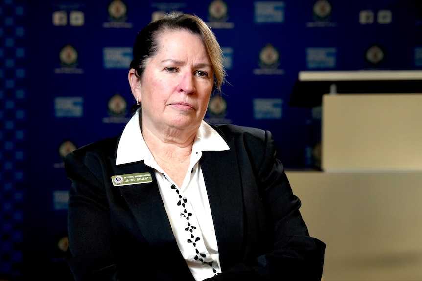 A middle-aged woman with short, dark hair with a blonde highlight wears a blazer and sits in front of a NSW Police backdrop.