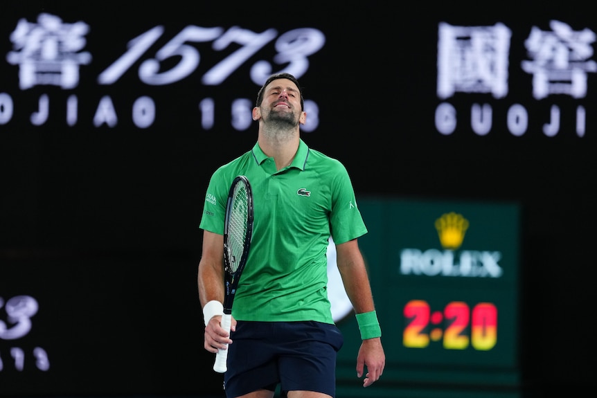 A tennis player in green throws his head back while smiling sheepishly 