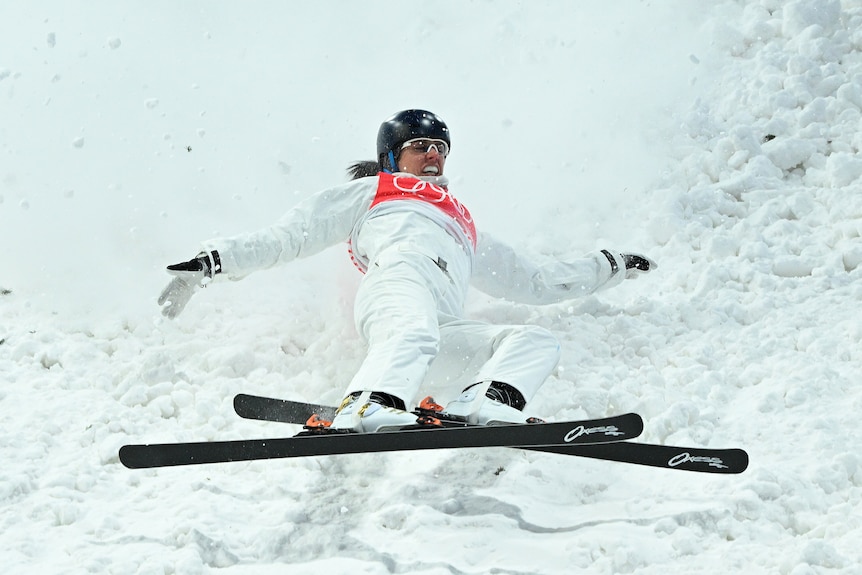 A skier falls backwards on to the snow, during a run down the slope.