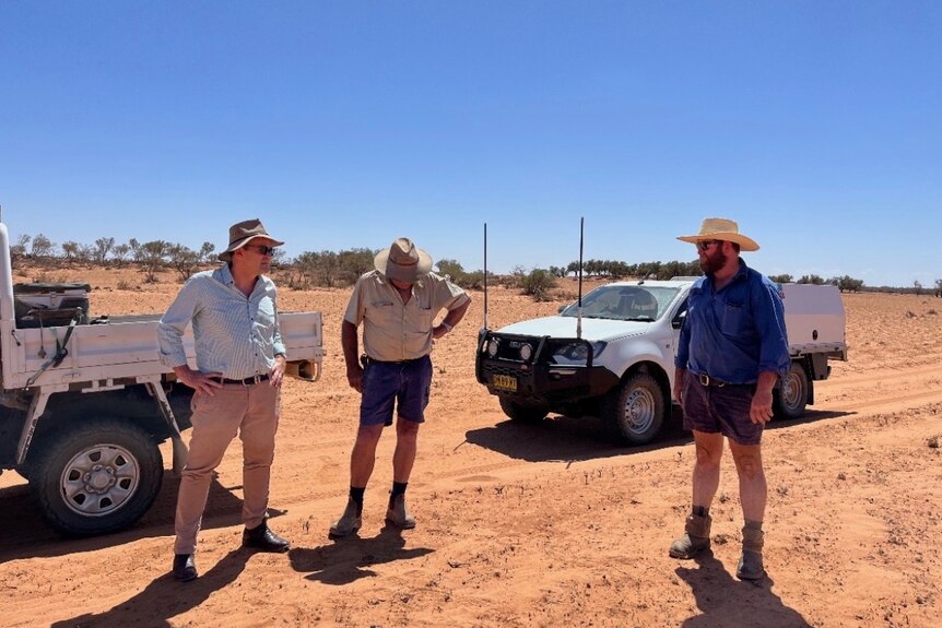 Three men in hats stand in a dry sandy landscape.