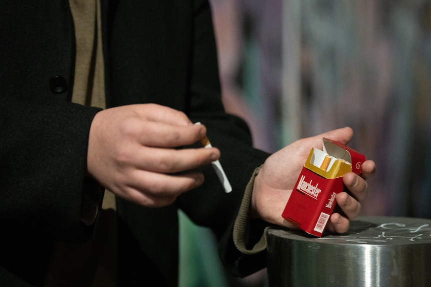 A man holding a red packet of cigarettes.