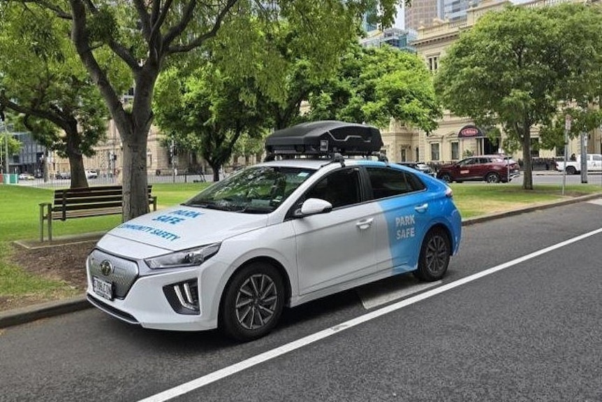 A sedan with words on the bonnet and back side door. A black box affixed to the top of the car parked on the street