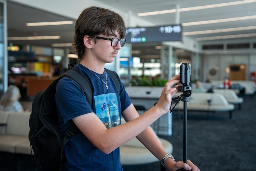 A man uses a phone on a tripod to take a photo at an airport gate