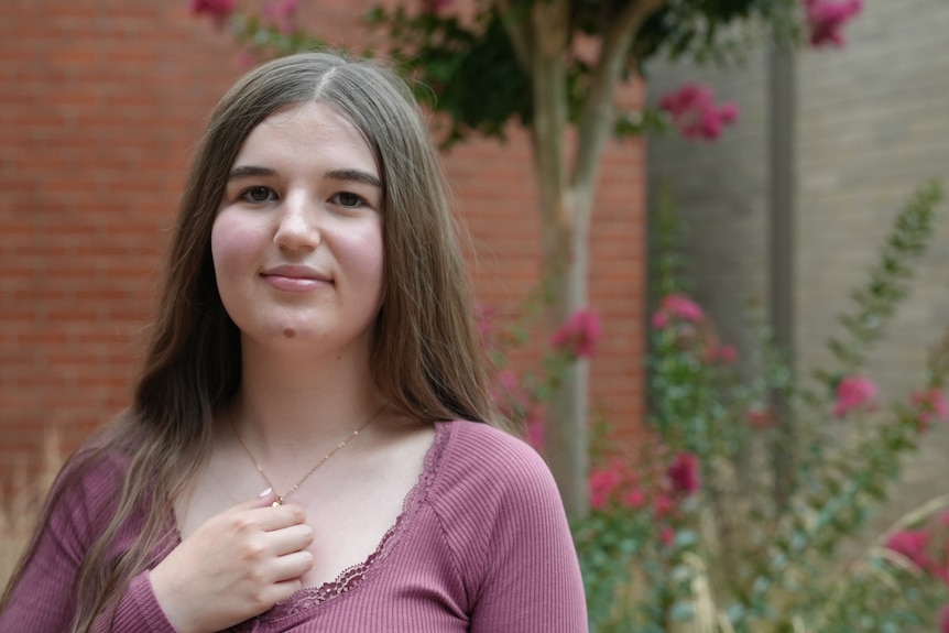 A young girl smiles and holds her chest.