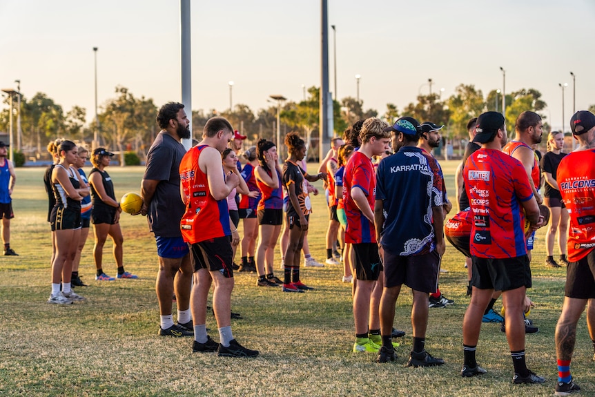 dozens of men and women in red and blue on a footy oval