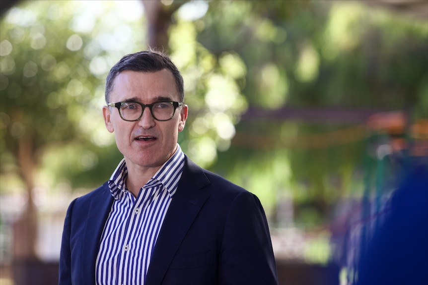 John Carey wearing glasses, dark jacket and striped shirt