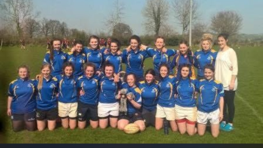 A women's rugby team poses for a photo, wearing blue jerseys.