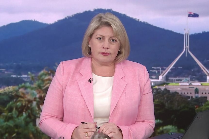 A woman in a pink jacket in a television studio.
