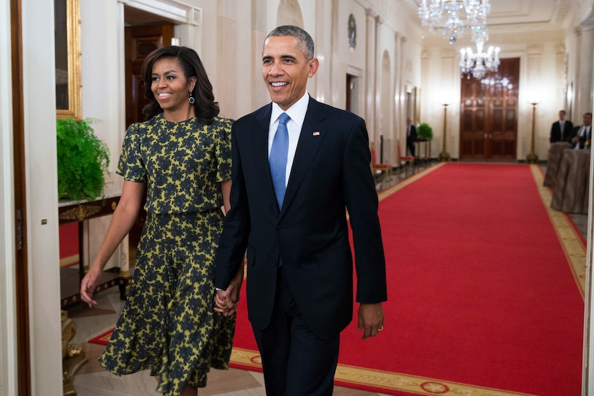 A man in a suit and a woman in a dress walk in a room with a red carpet.