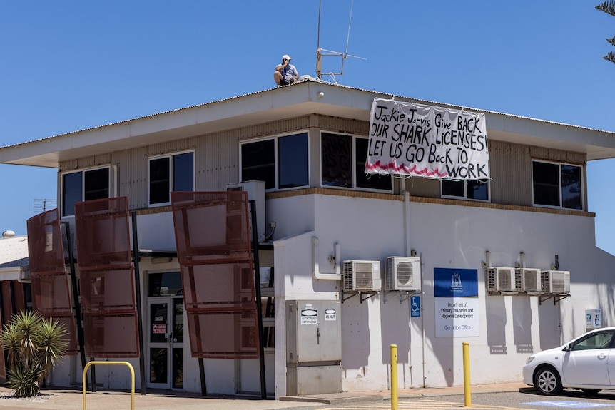 Longer shot of the DPIRD building, with John Higham visible on roof and his protest sign hanging from the gutter.