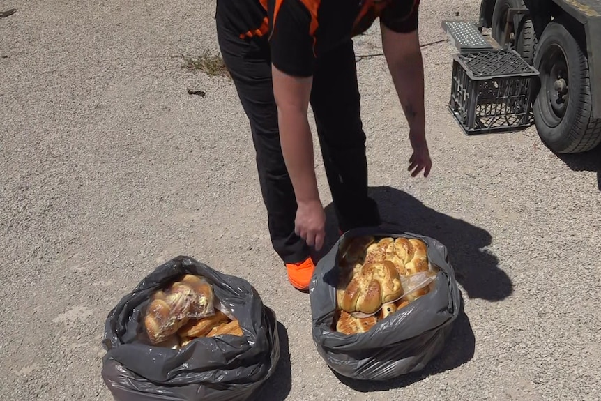 Two black garbage bags filled with bread rolls on the concrete ground