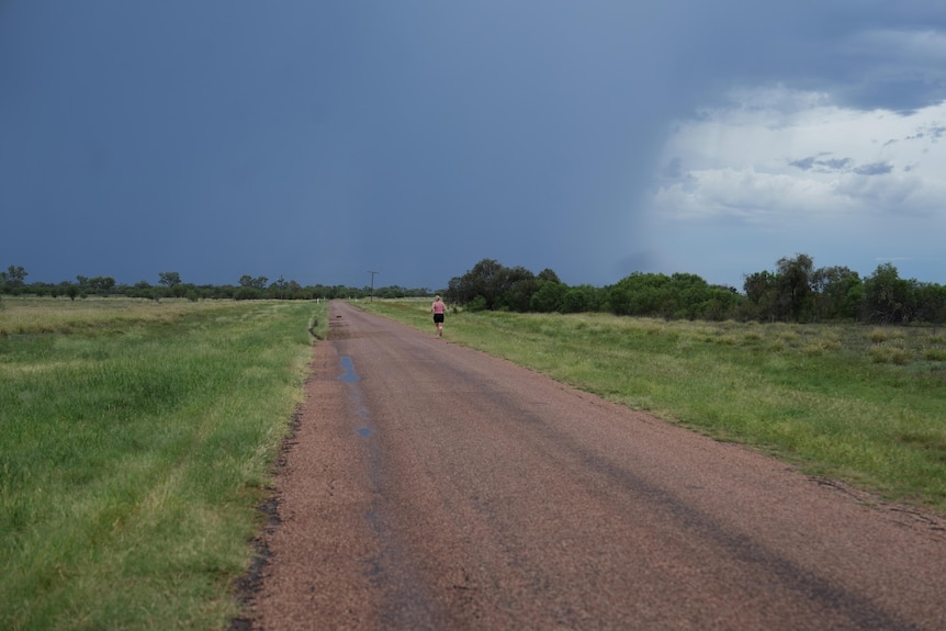 A young woman down a country road with dark storm clouds looming ahead.