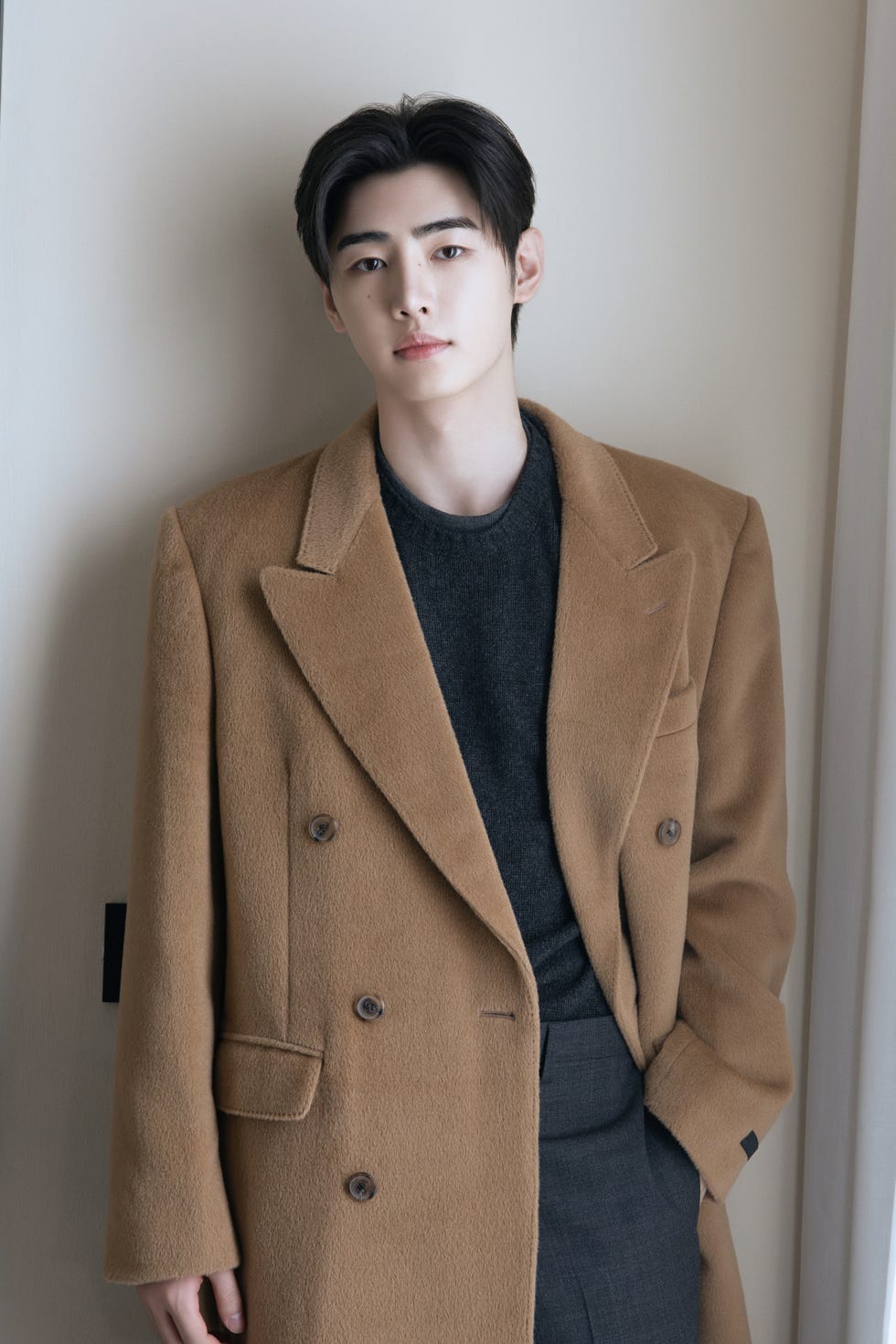 Individual wearing a stylish brown coat over a dark sweater.