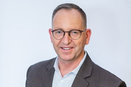 A professional headshot of a man. He has is dressed professionally and smiles looking at the camera.