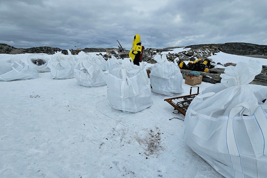 Large white bags full of waste sit ready on snowy ground to be collected by a helicopter