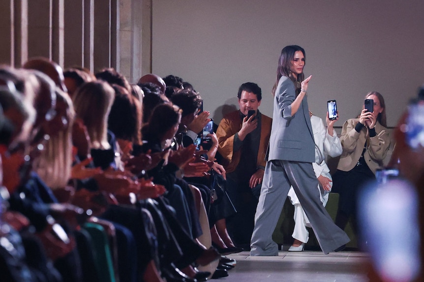 Designer Victoria Beckham waves at attendees during the presentation of a fashion collection. 