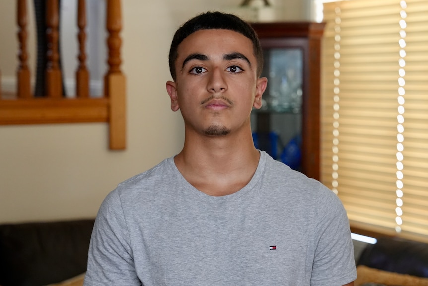 Teenager Nadel looks seriously at the camera while wearing a grey shirt.