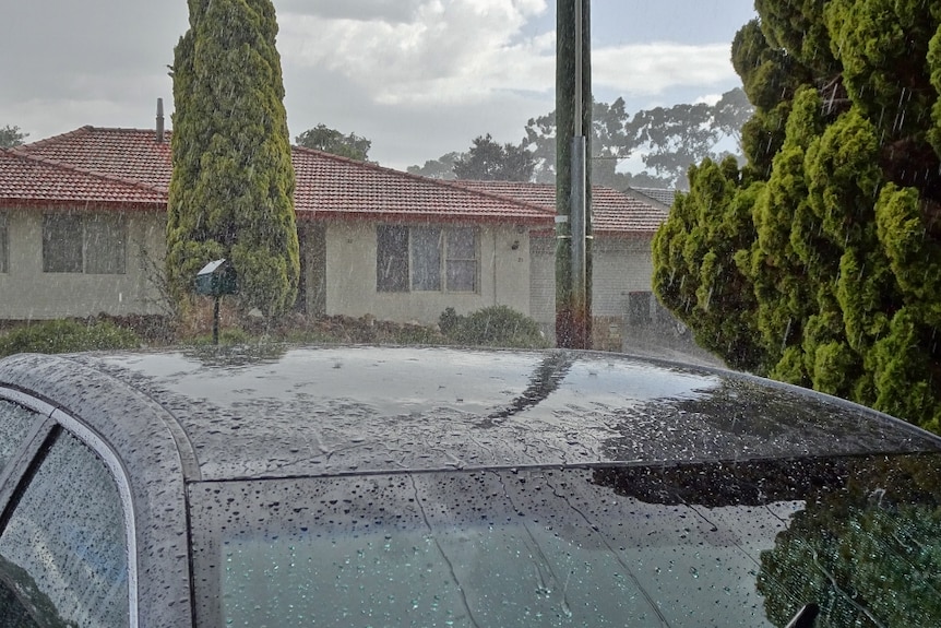 Rain pelts the roof of a car pictured in front of a house