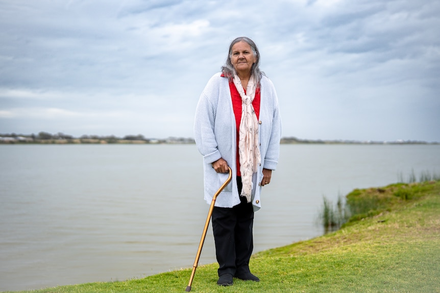 A woman with a walking stick on grass by a river