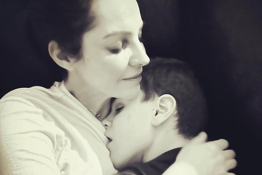 A man is cuddling her son sitting on a sofa