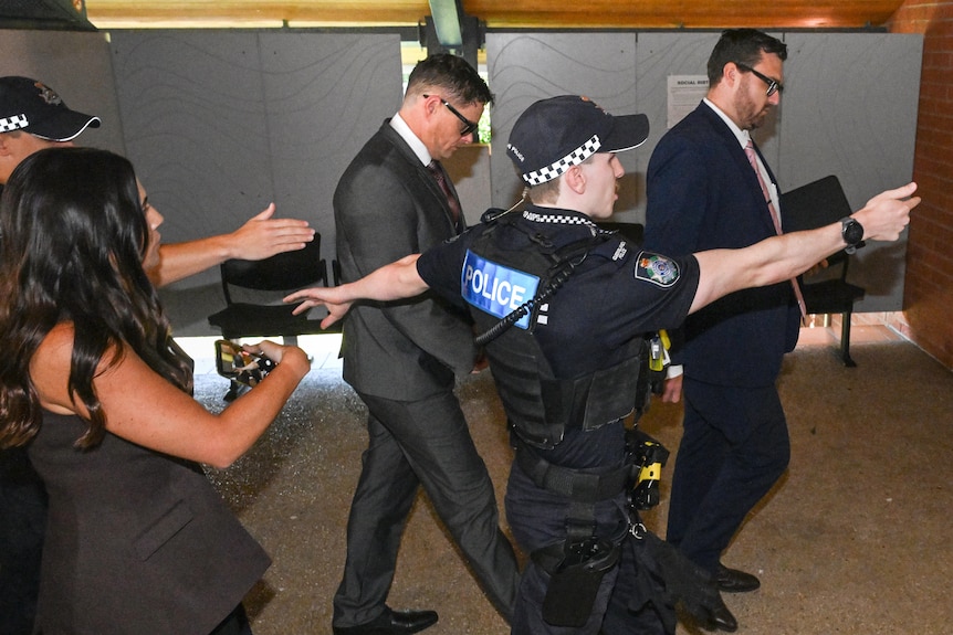 A man walking with police around him